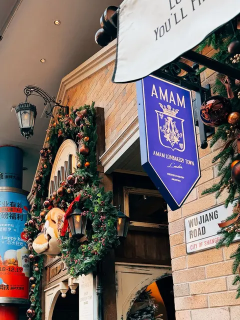 Mặt tiền gạch nâu của AMAM LONBAKERY TOWN, biển treo hình khiên màu xanh 'AMAM LONBAKERY TOWN London' và biển trắng 'WUJIANG ROAD · CITY OF SHANGHAI', cửa trang trí vòng hoa Giáng Sinh