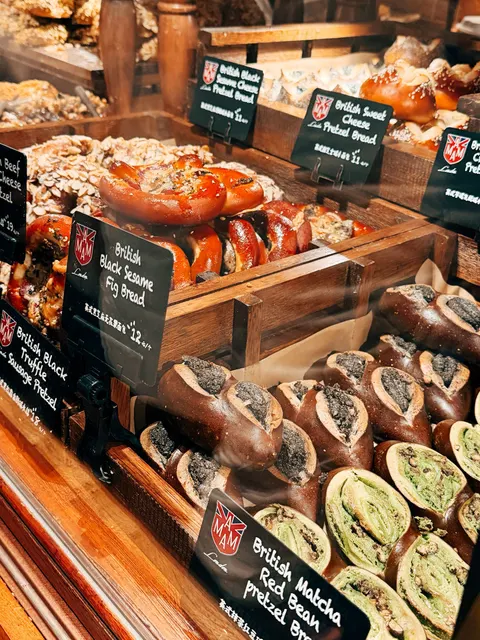 Kệ gỗ bày bánh pretzel nhồi nhân, bảng tên 'British Black Sesame Fig Bread' và 'British Sweet Cheese Pretzel Bread'