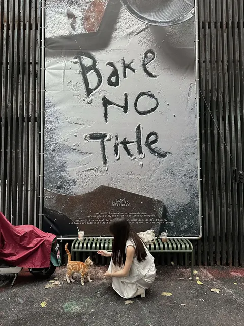 Mặt tiền Bake No Title ở 番禺路232号: tấm biển lớn nền xám thô với chữ 'Bake NO Title' viết tay, xung quanh là thanh gỗ dọc và băng ghế xanh