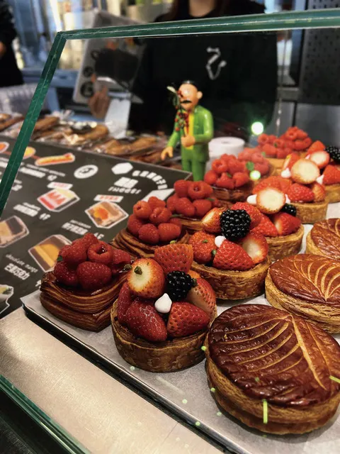 Tủ kính bày các loại bánh tart trái cây và bánh galette des rois tại quầy BAsdBAN, có hình nhân vật đồ chơi trang trí