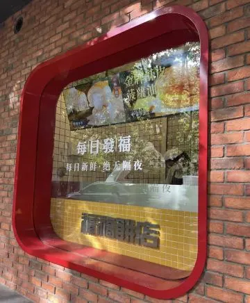 Biển tròn khung đỏ trên tường gạch đỏ ghi '福福餅店 · 每日新鲜 · 绝无隔夜' (tươi mỗi ngày, không bán bánh qua đêm)