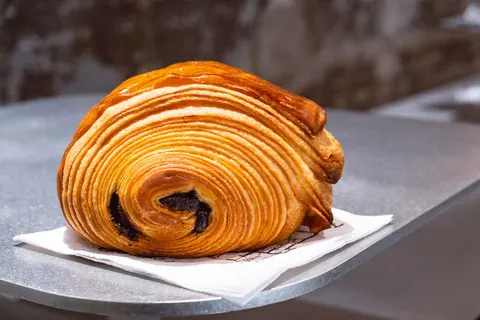 Một chiếc bánh sừng bò lớn nhiều lớp vàng óng của BAsdBAN, lộ nhân socola, đặt trên đĩa kim loại