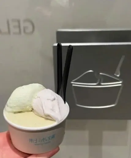 Cốc gelato 制冰铺 hai vị xanh nhạt và tím nhạt, hai que đen, phía sau là logo bát kem kim loại