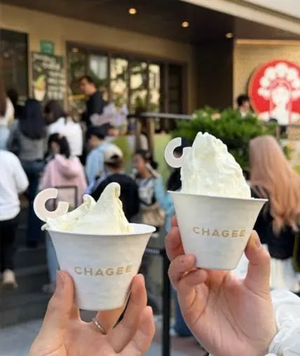 Hai tay cầm hai cốc gelato trắng in chữ CHAGEE trước cửa hàng
