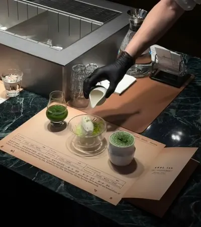 Pha chế viên đeo găng rót sữa bên ly matcha, đặt trên tấm thẻ nếm in chữ AKAL lab của quán (ảnh An gửi, 08/10)