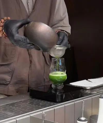 Pha chế viên AKALCHA đeo găng đen rót trà qua rây vào ly matcha đặt trên cân, ngay tại quầy (ảnh An gửi, 08/10)