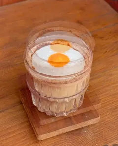 Một ly cà phê lớp kem trắng, giữa có vòng tròn cam như lòng đỏ trứng, đặt trên đế gỗ — Metal Hands (ảnh An gửi)