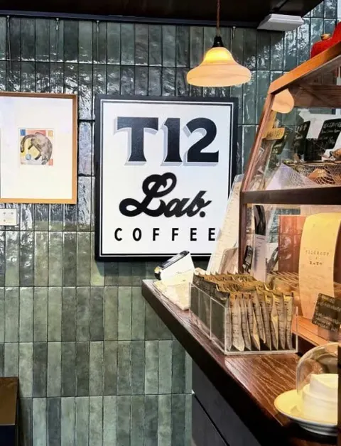 Biển T12 Lab COFFEE trên tường gạch xanh, quầy gỗ bên dưới (ảnh An gửi)