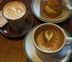 Latte ly thủy tinh, cappuccino và bánh scone trên bàn gỗ tròn ở T12 Lab (ảnh An gửi)