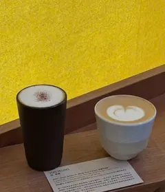 Ly cà phê đen và tách latte vẽ hình trái tim trên khay gỗ, tường vàng — 3½ (ảnh An gửi)