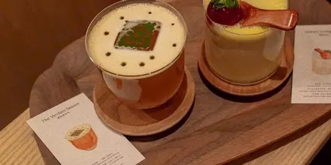 Hai món trên khay gỗ ở Leaf Sòng: ly trà sữa phủ bột trà xanh và ly kem vàng có dâu tây, cạnh tấm thẻ giới thiệu món