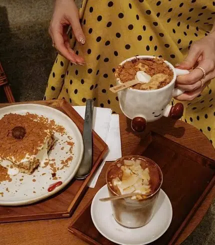 Đĩa tiramisu và ly cà phê đá đặt trên khay gỗ ở Plusone
