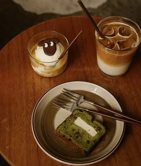 Bàn gỗ tròn ở Blacksheep Espresso: ly affogato có bánh quy hình chú cừu đen, ly latte đá và đĩa bánh trà xanh nhân đậu đỏ