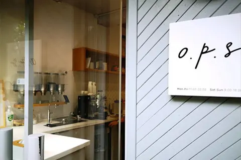 Mặt tiền O.P.S CAFE trên đường Thái Nguyên, cửa gỗ xám mở ra quầy pha chế, biển hiệu 'o.p.s' và giờ mở cửa dán trên tường