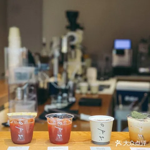 Bốn ly đồ uống đặc chế xếp hàng trên quầy O.P.S, phía sau là máy xay cà phê và dụng cụ pha chế