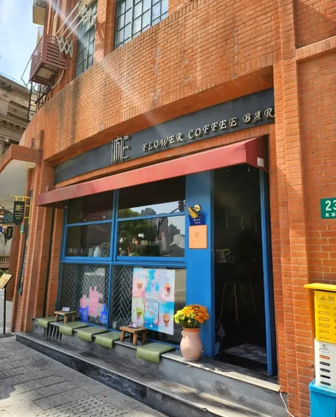 Mặt tiền gạch đỏ của 汭·FLOWER COFFEE BAR trên đường Bắc Tô Châu, cửa kính xanh, bình hoa cúc vàng trước cửa