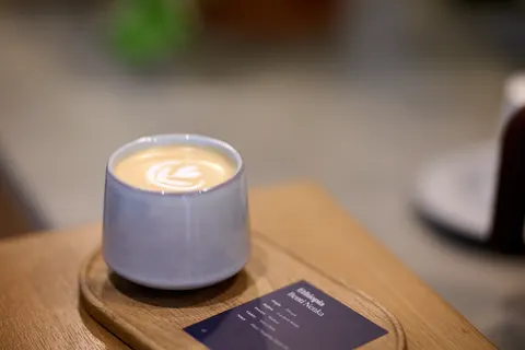 Ly cà phê đặc chế tại Spot Table với hình vẽ latte art hình lá, đặt trên khay gỗ kèm thẻ giới thiệu nguồn gốc hạt cà phê Ethiopia