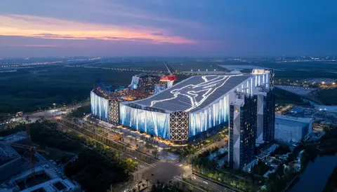Toàn cảnh khu nghỉ dưỡng trượt tuyết trong nhà nhìn từ trên cao lúc chạng vạng, toà nhà lớn sáng đèn bên đường lớn (ảnh: 澎湃新闻 The Paper, do đơn vị thiết kế khu trượt tuyết cung cấp)