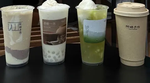 Bốn ly trà sữa 阿嬷手作 xếp hàng trên bàn: ly mochi khoai môn, ly có trân châu trắng và kem, ly trà xanh đá, ly cốc giấy in chữ 阿嬷手作 (ảnh An gửi)