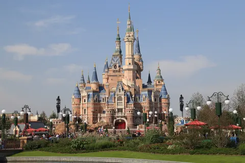 Lâu đài Enchanted Storybook Castle của Shanghai Disneyland nhìn từ phía trước, nhiều tháp nhọn mái xanh dương, xung quanh là vườn hoa và du khách