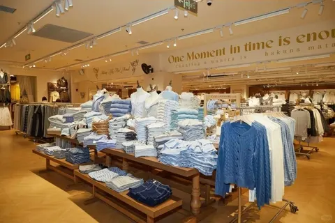 Bên trong tiệm ONE MOMENT ở 淮海百盛 (đường Hoài Hải): bàn gỗ xếp áo trắng và xanh, tường có dòng chữ 'One Moment in time is enough' — tiệm khác, không phải tiệm GATE M (ảnh: 赢商网)