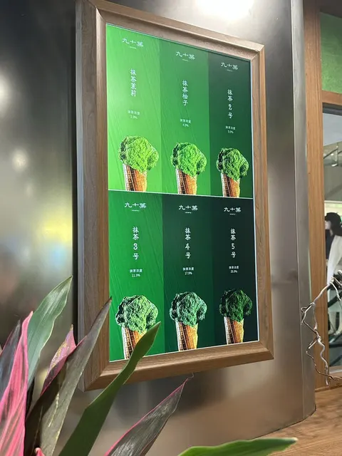 Bảng menu các cấp độ trà xanh matcha treo trên tường, trang trí cây xanh bên cạnh