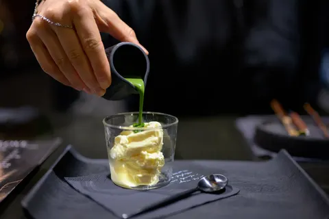 Matcha affogato — một dòng matcha xanh đang được rót lên viên kem vanilla trong ly thủy tinh nhỏ