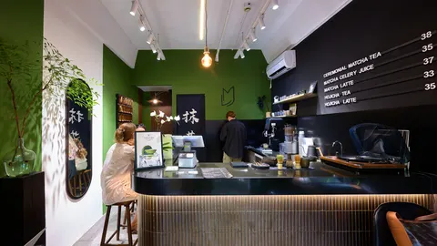 Quầy pha chế Matcha Love với tường xanh lá, bảng giá viết tay và nhân viên đang pha chế