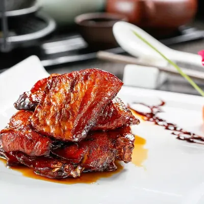 Món thịt kho kiểu bản bang sốt đậm màu cánh gián, xếp từng miếng trên đĩa trắng