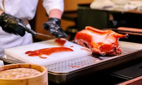 Đầu bếp đeo găng tay đen lọc vịt quay nguyên con ngay tại bàn, da vịt bóng đỏ