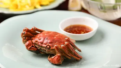 Một con cua lông hấp nguyên con (清蒸大闸蟹) bày trên đĩa sứ men ngọc, kèm chén nước chấm gừng giấm