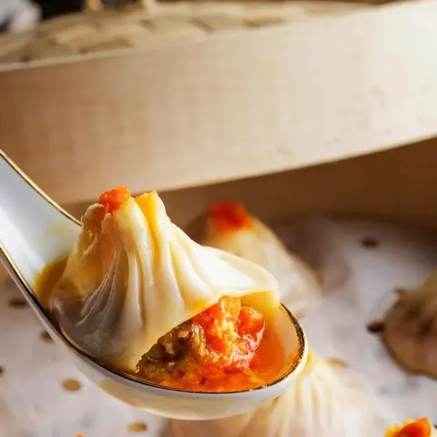 Bánh bao hấp nhân gạch cua (蟹粉小笼包) được gắp bằng thìa, lộ lớp nhân gạch cua màu cam