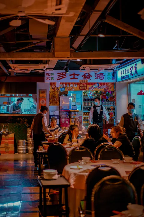 Phòng ăn của Lầu Thượng chi nhánh Nam Hối: trần lộ dầm gỗ và quạt trần, bảng hiệu kiểu tiệm tạp hoá Hồng Kông xưa, bàn tròn trải khăn trắng