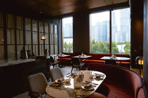Phòng ăn chính của Meet The Bund chi nhánh BFC: trần ốp gỗ tối, quầy đá cẩm thạch, cửa kính lớn nhìn ra cây xanh và nhà cao tầng