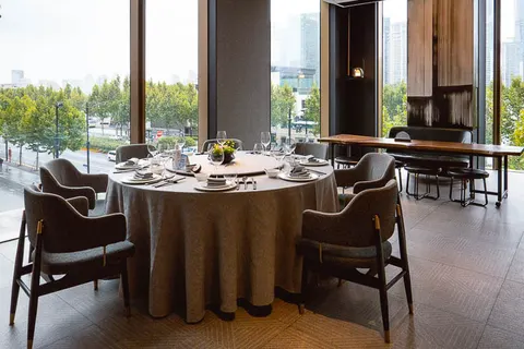 Phòng riêng của Meet The Bund với bàn tròn phủ khăn và tường kính nhìn ra phố