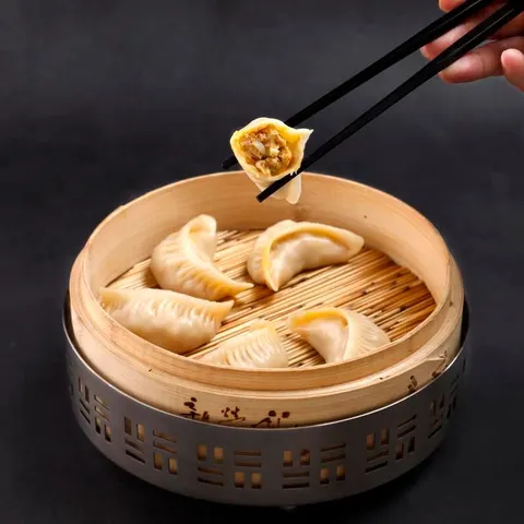 Bánh hấp trong xửng tre, một chiếc được gắp lên bằng đũa đen