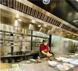 Bếp mở inox của tiệm, nhân viên đeo khẩu trang đang chuẩn bị đồ ăn