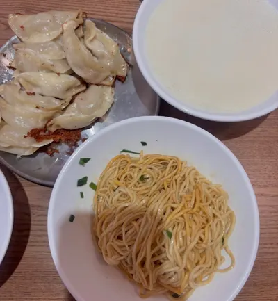 Một đĩa 煎饺, bát mì trộn rắc hành và bát trông như sữa đậu trên bàn gỗ; ảnh không cho biết chi nhánh (ảnh An gửi, 08/10)