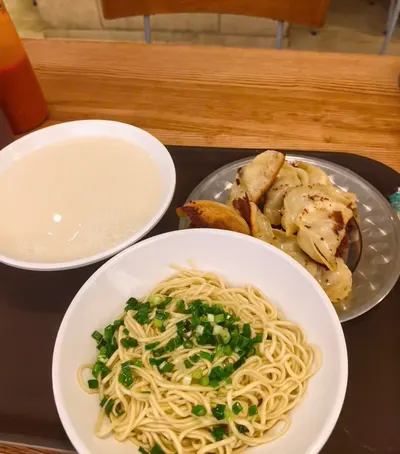 Khay ăn sáng gồm đĩa 煎饺 đáy chiên vàng, bát mì trộn phủ nhiều hành lá và bát trông như sữa đậu; ảnh không cho biết chi nhánh (ảnh An gửi, 08/10)