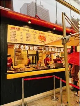 Quầy 泮芳春煎饺 chi nhánh 889广场: mái hiên đỏ, bảng giá vàng phía trên và bếp mở ngay sau quầy kính