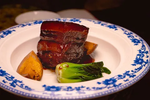 Phần 红烧肉 riêng: miếng ba chỉ kho bóng màu nâu đỏ, kèm trứng và cải thìa trên đĩa viền hoa xanh