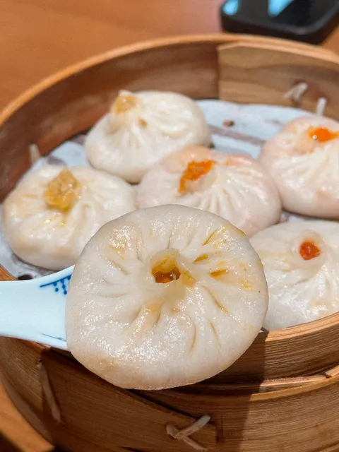 Cận cảnh một chiếc tiểu long bao gạch cua được gắp lên bằng muỗng sứ, lộ rõ nhân gạch cua màu cam bên trong