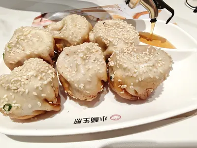Một đĩa sinh tiền (生煎) vàng giòn đáy, rắc vừng và hành lá, bên cạnh bình giấm đang rót — ảnh khách trên Dianping, chụp tại 小杨生煎 宁波路店