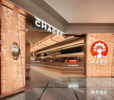 Lối vào quầy 'TEABAR' của 霸王茶姬 CHAGEE với biển đèn CHAGEE và logo tròn đỏ trên tường ốp đồng, không gian tông ấm tại flagship 美罗城
