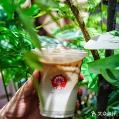 Ly trà sữa CHAGEE có logo tròn đỏ in trên cốc, nền cây xanh tự nhiên