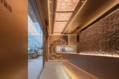 Quầy phục vụ nhìn ra cửa kính của flagship 霸王茶姬 美罗城, tường ốp đồng và mảng trang trí khảm gốm hình trăng khuyết