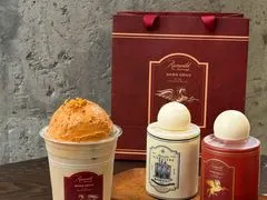 Cốc trà phủ kem đặt cạnh hai hộp quà tròn màu đỏ có ruy băng, bày cùng túi giấy in logo CHUNTIAN