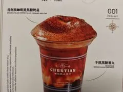 Cốc trà sữa đen phủ mè rang vàng, thẻ món trên quầy ghi số hiệu '001 PROJECT' của quán