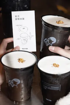 Ba ly trà sữa phủ bọt kem đặc trưng cạnh thẻ món 'Nham Lan ·崇明米酿' viết tay của Tea Lab, một ly có in logo heytea lab