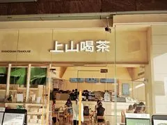 Mặt tiền 上山喝茶 SHANGSHAN TEAHOUSE với biển hiệu chữ nâu trên nền gỗ sáng, cửa kính mở ra không gian ngồi ấm áp bên trong
